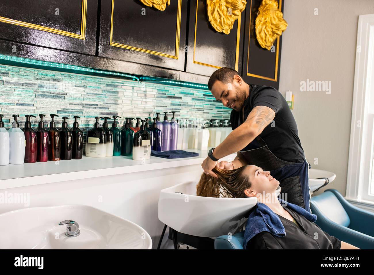 Stylist washing young woman’s hair in sink at boutique salon Stock Photo