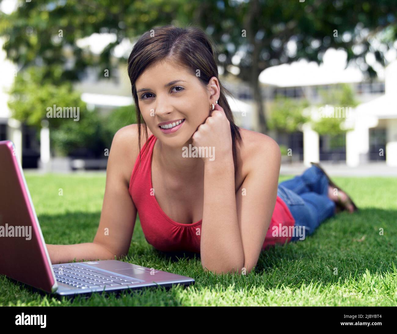 Female student lying on grass using her laptop computer Stock Photo