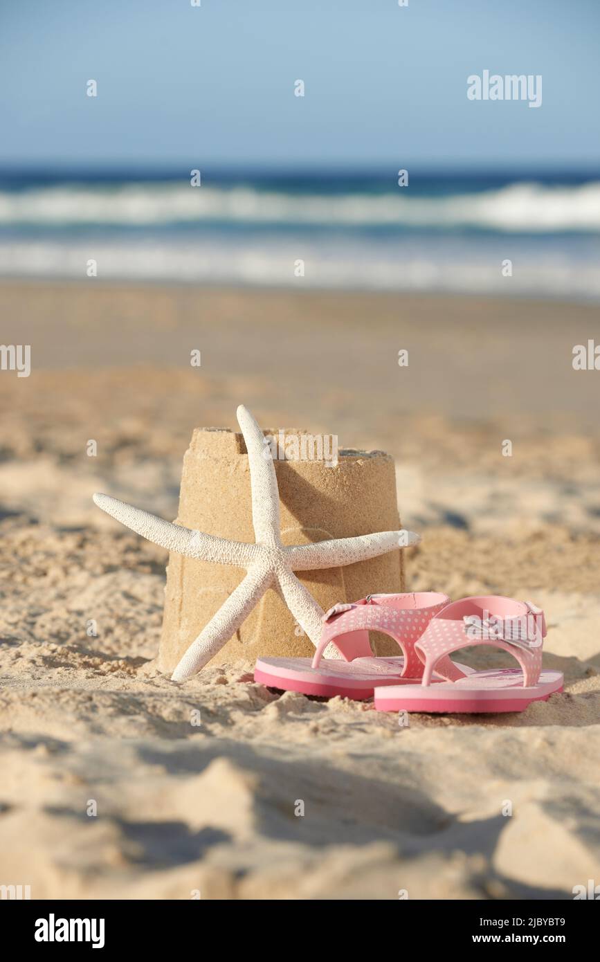 Flip flops and starfish next to sandcastle on the beach Stock Photo - Alamy