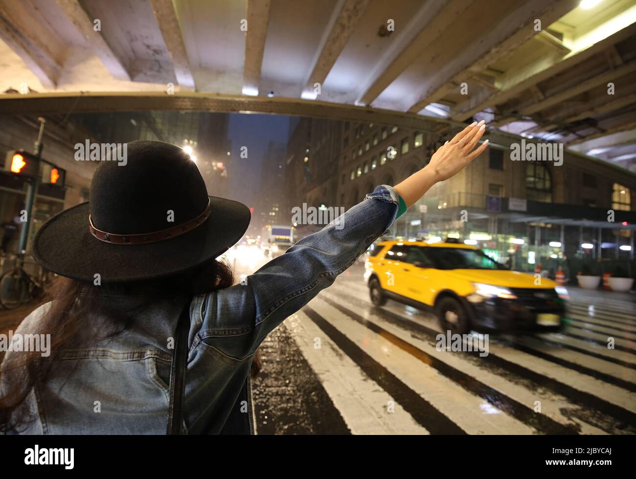 Beautiful Fashionable young woman hailing a taxi on 42nd Street outside Grand Central Station on a rainy stormy night, Manhattan, New York City, NY Stock Photo