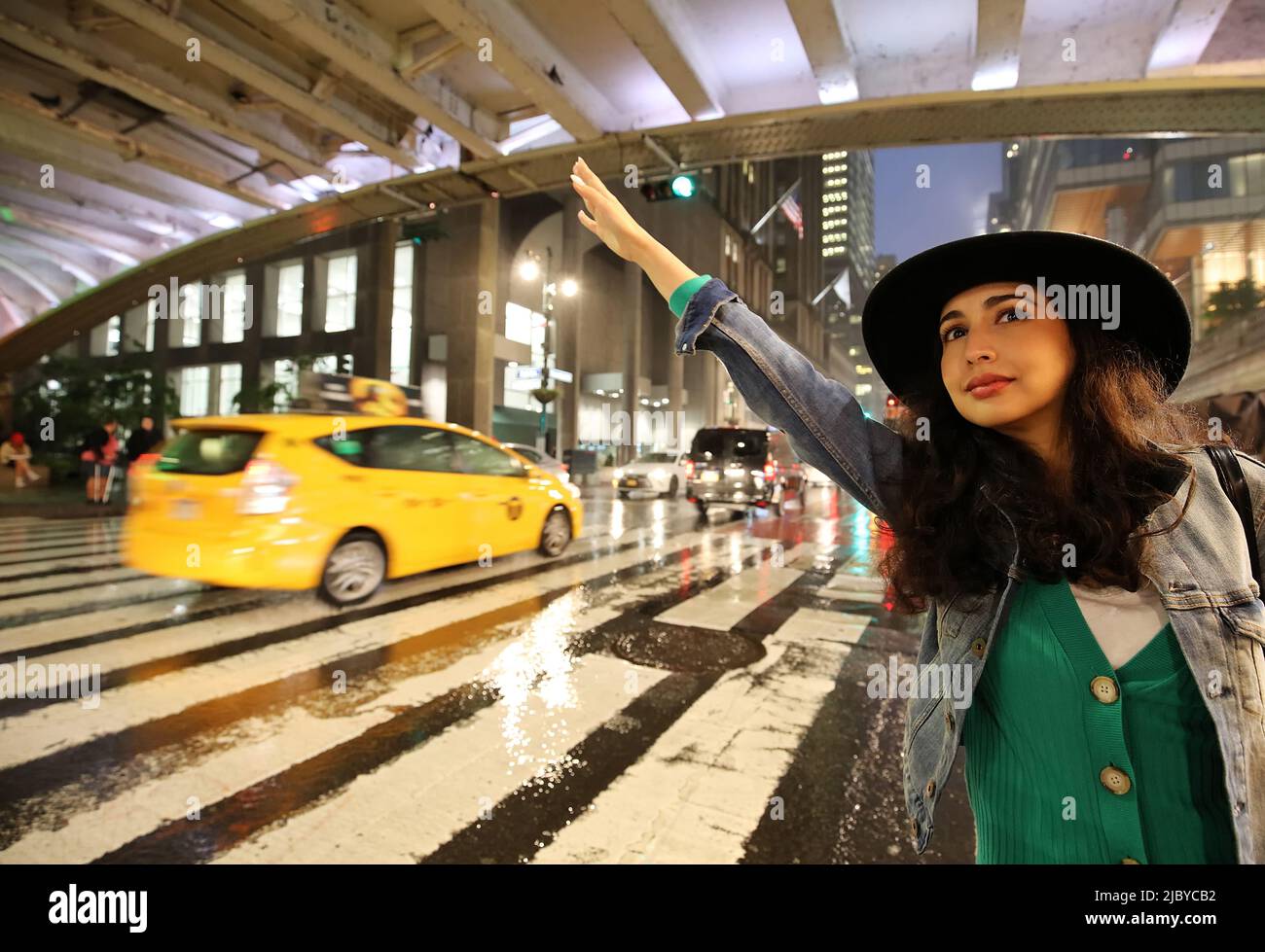Beautiful Fashionable young woman hailing a taxi on 42nd Street outside Grand Central Station on a rainy stormy night, Manhattan, New York City, NY Stock Photo