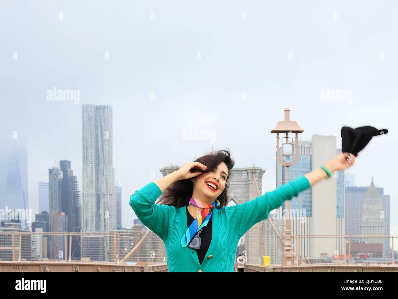 Beautiful female tourist happy dancing on the Brooklyn Bridge, with New York City Skyline in the background - Manhattan, New York City, New York, USA Stock Photo