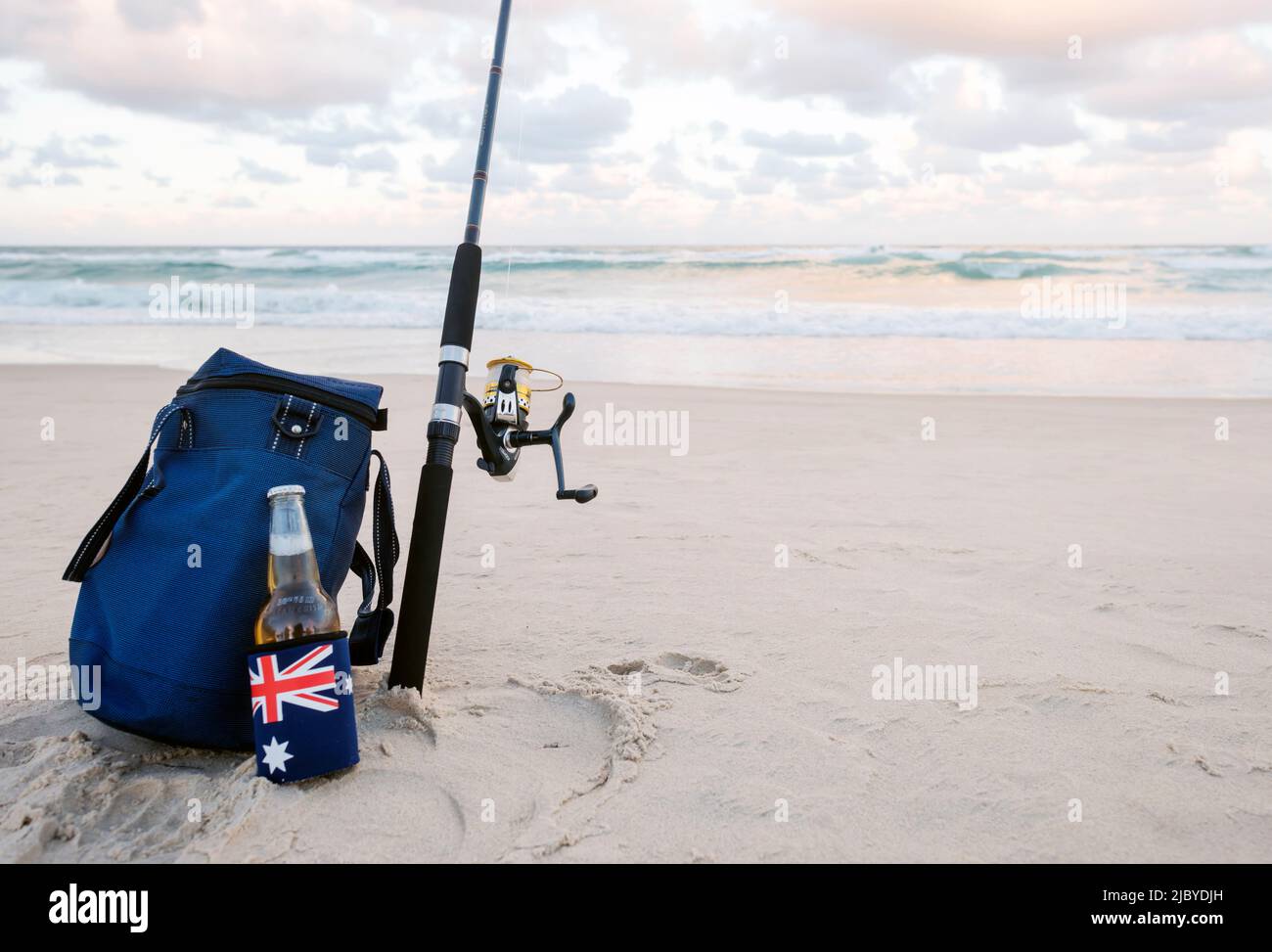 Beer in stubbie holder with Australian Flag, cooler bag and Fishing Rod on the sand at the beach Stock Photo