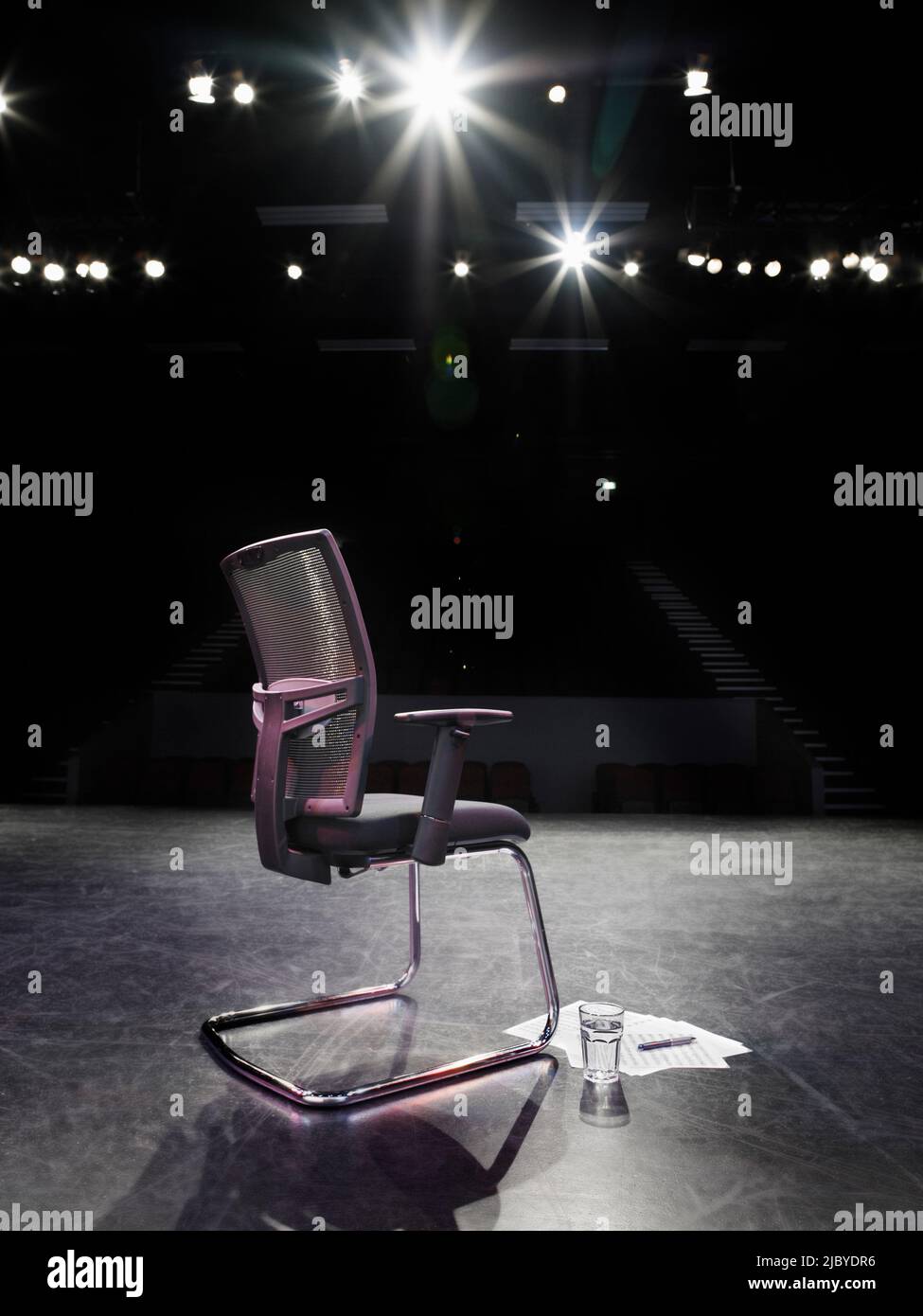 Back view of spotlit empty chair on stage with script and glass of ...