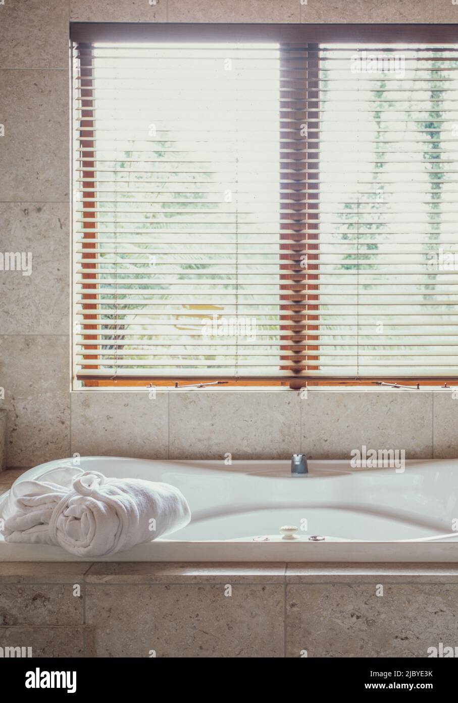 Luxury spa bath surrounded by marble underneath window in bathroom