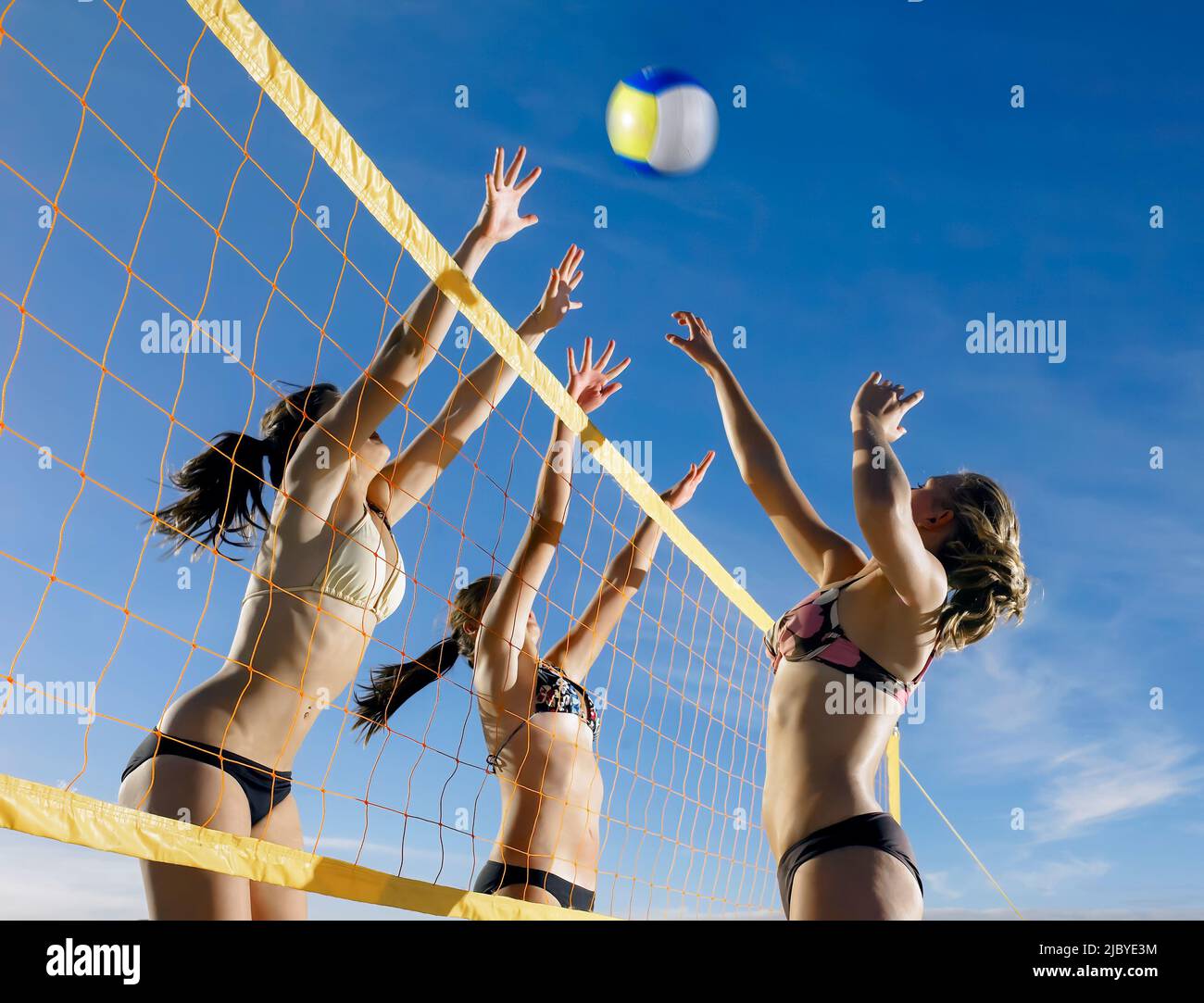 Young women on opposing teams jumping to hit the ball over the net in