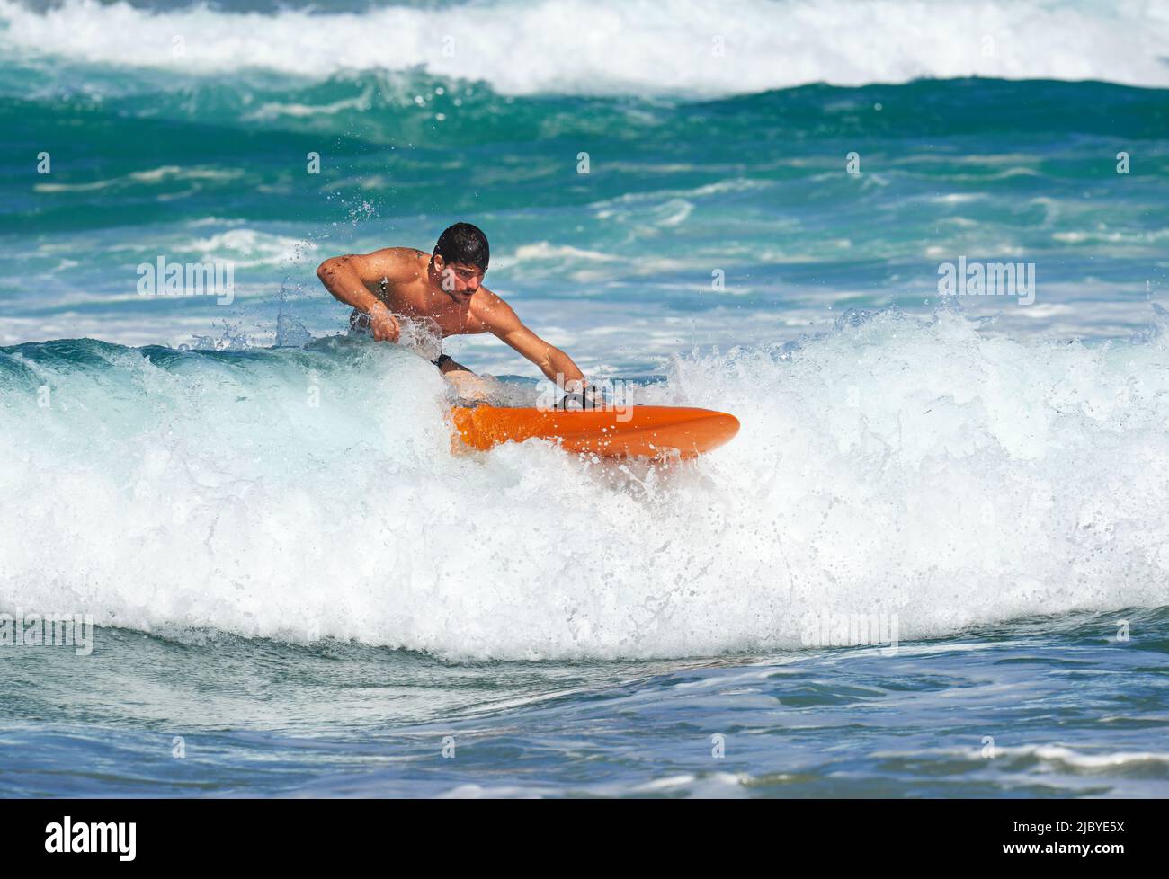 Male Surf Lifesaver riding a wave on ocean surf ski Stock Photo
