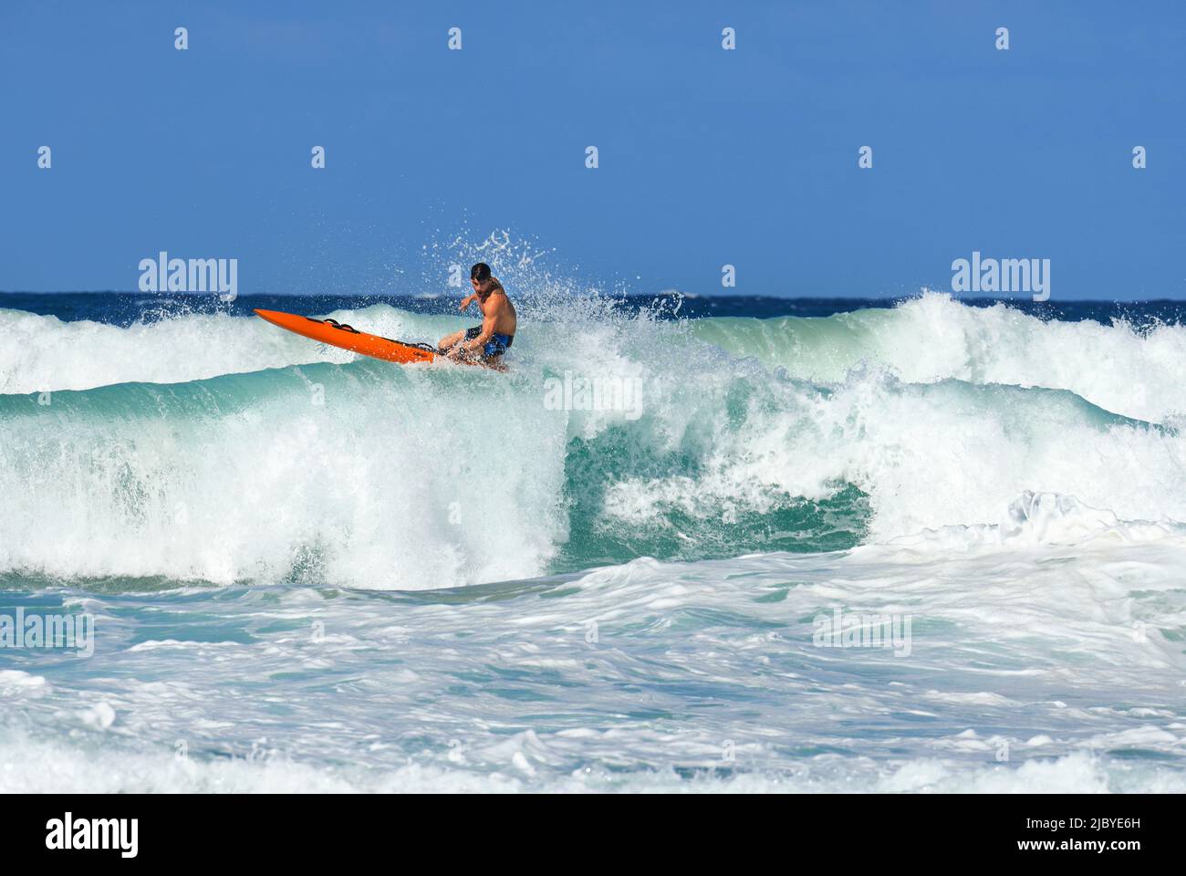 Male Surf Lifesaver riding a wave on ocean surf ski Stock Photo
