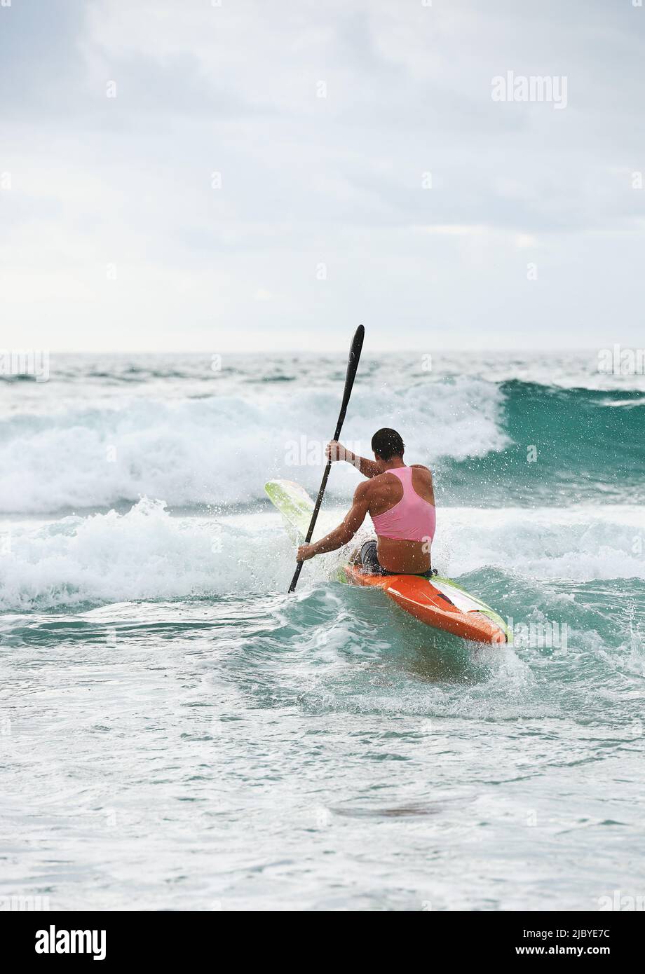 Back view of male surf lifesaver paddling through waves on ocean surf ski Stock Photo