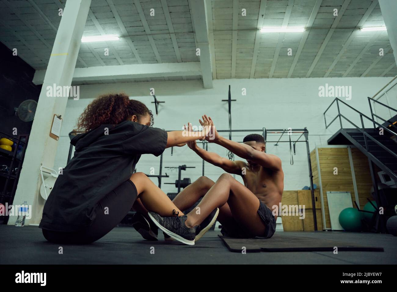 Mixed race friends doing cross fit in the gym. Male personal trainer giving African American female a high-five after exercising. High quality photo Stock Photo