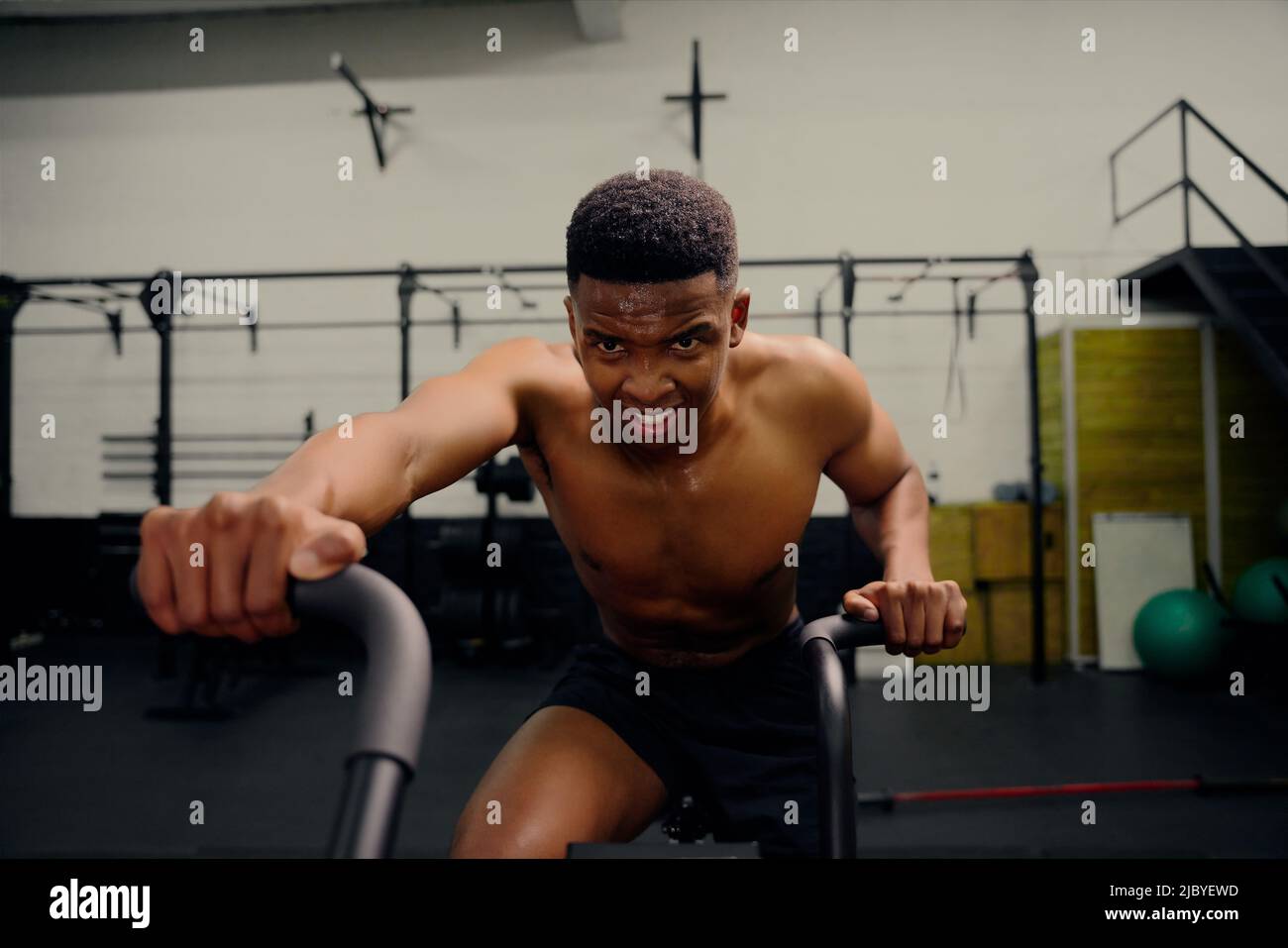 https://c8.alamy.com/comp/2JBYEWD/african-american-male-using-an-elliptical-trainer-during-cross-fit-training-male-athlete-exercising-intensely-in-the-gym-high-quality-photo-2JBYEWD.jpg