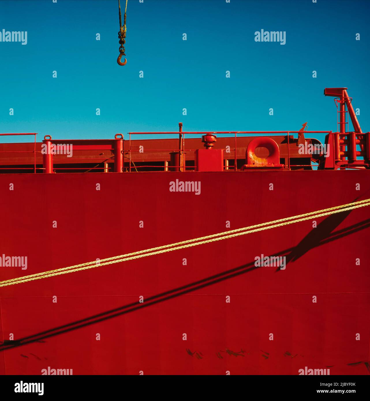 Crane Hook against blue sky decending to red ship tied to dock at Port