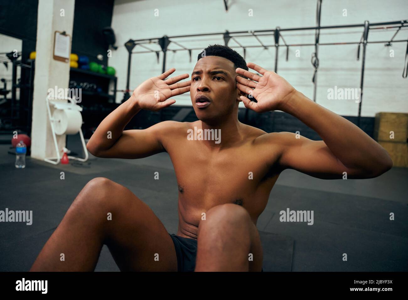 Young, topless African American male doing sit-ups on the floor in the gym. Mixed race male personal trainer doing cross training indoors. High Stock Photo