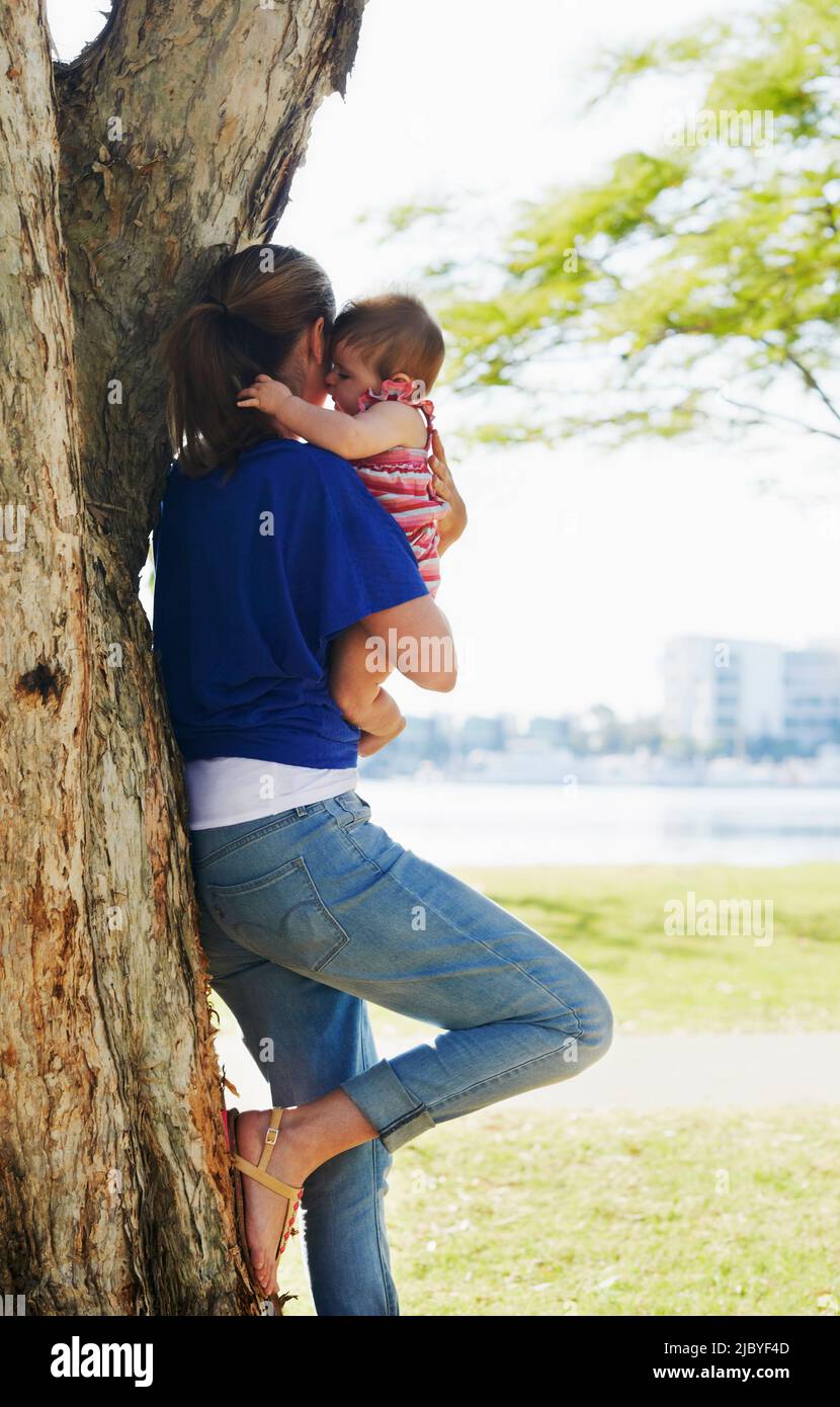 Mother leaning against tree holding baby at park Stock Photo Alamy
