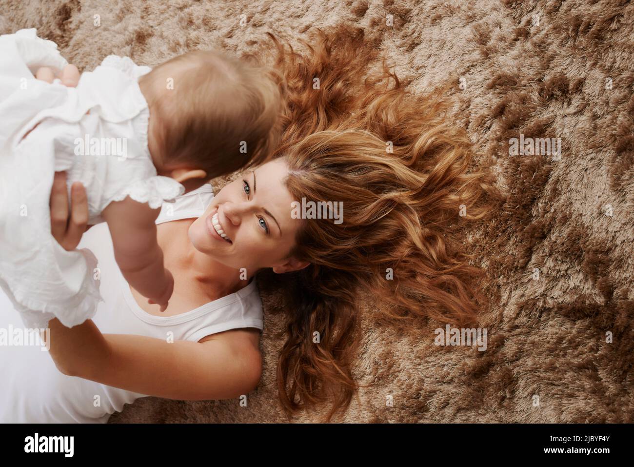 Mother laying on the floor and holding baby up and smiling Stock Photo