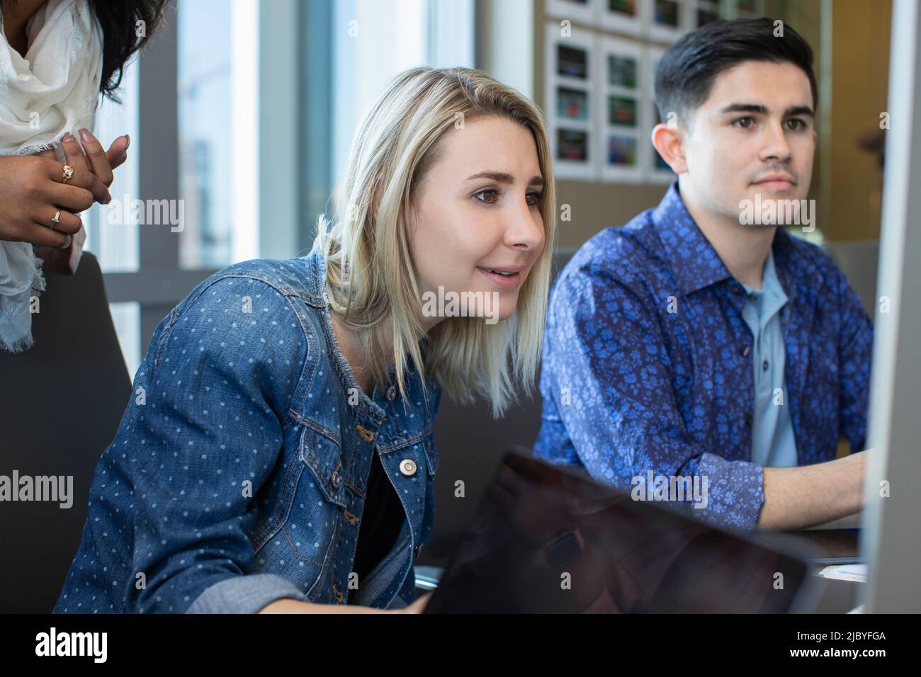 Young woman using computer in office, showing co-workers something on her screen Stock Photo