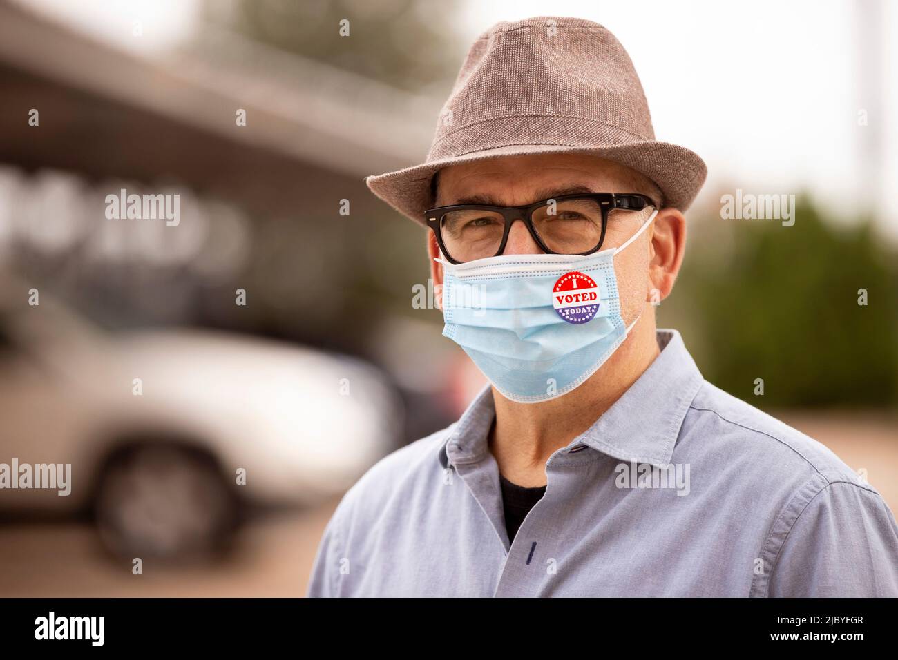 Older Caucasian male with glasses and fedora, wearing a mask and an I Voted Today sticker on the mask Stock Photo