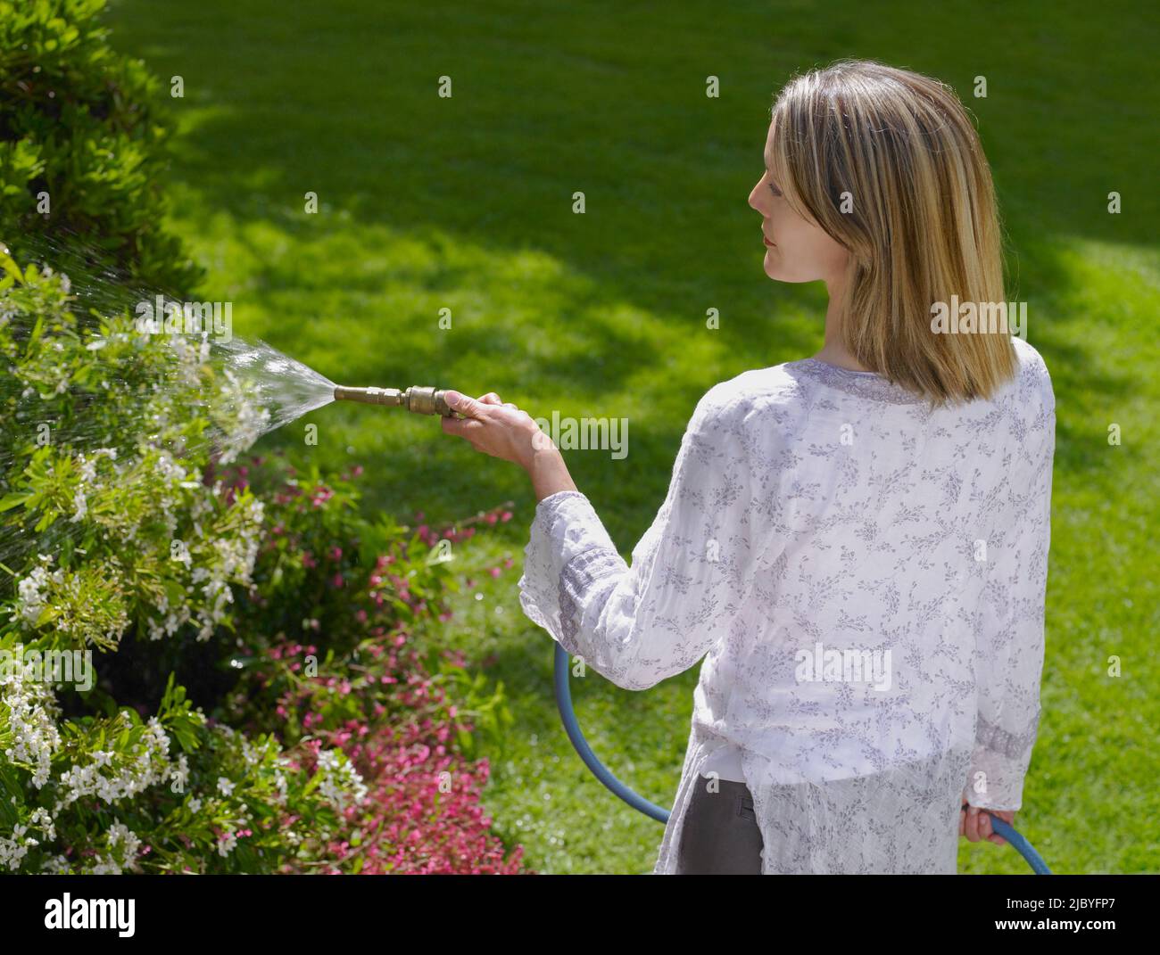 Woman watering flowering plants in her garden Stock Photo - Alamy
