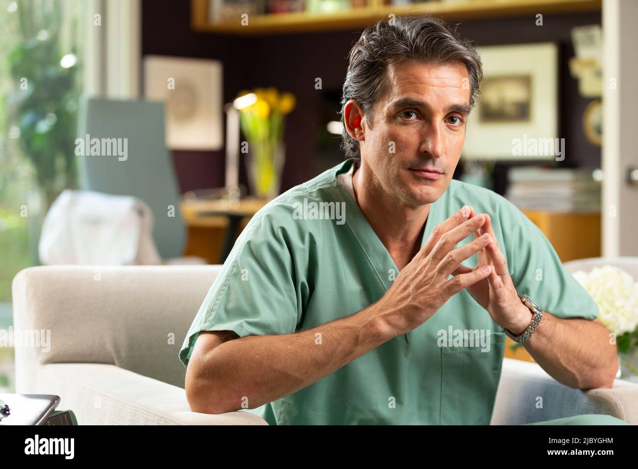 Portrait of Hispanic Male doctor sitting in his home office, taking a break from practicing Tele-medicine Stock Photo