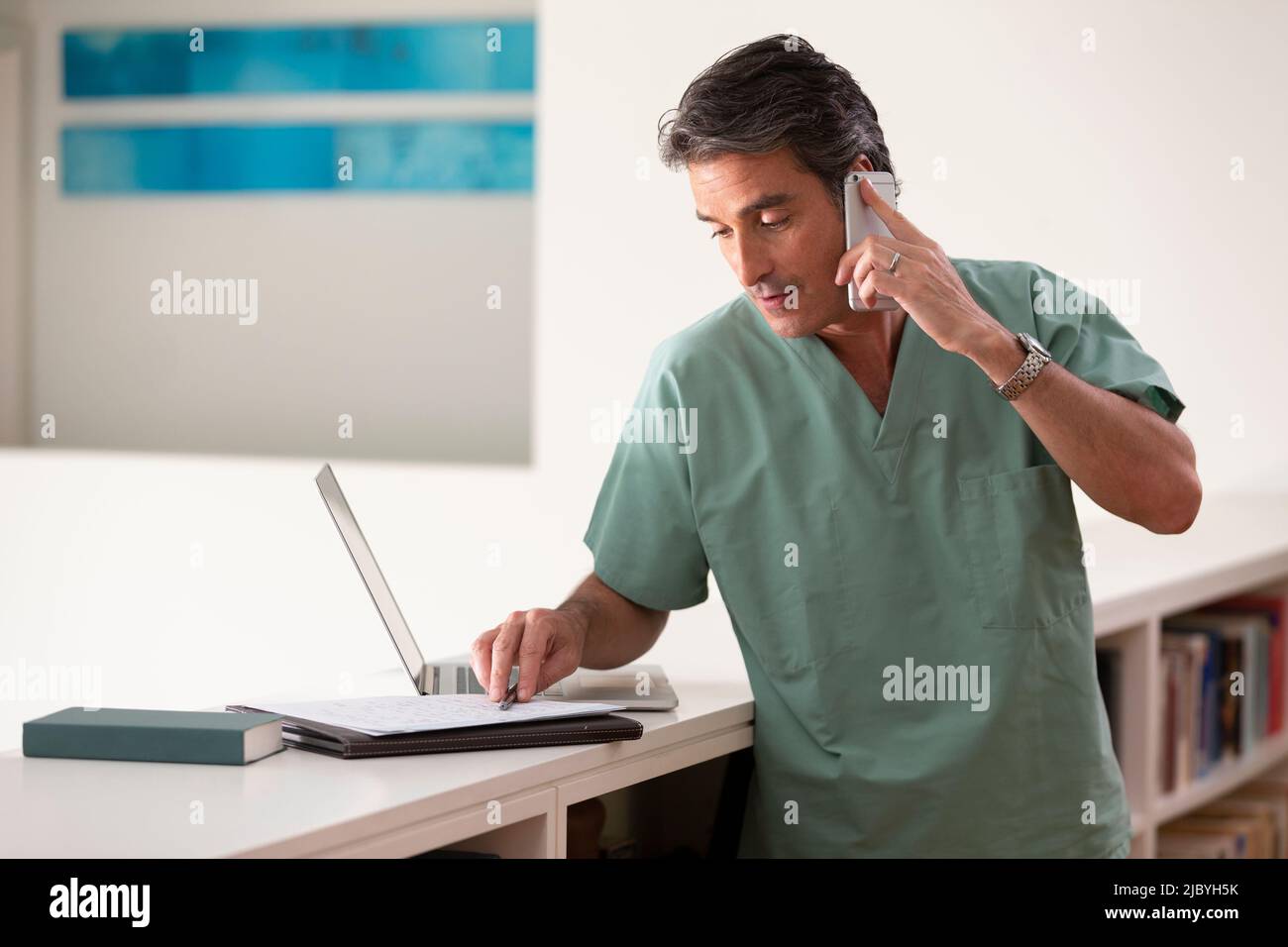 Hispanic Male doctor in his home practicing Telemedicine, talking on cell phone and taking notes Stock Photo