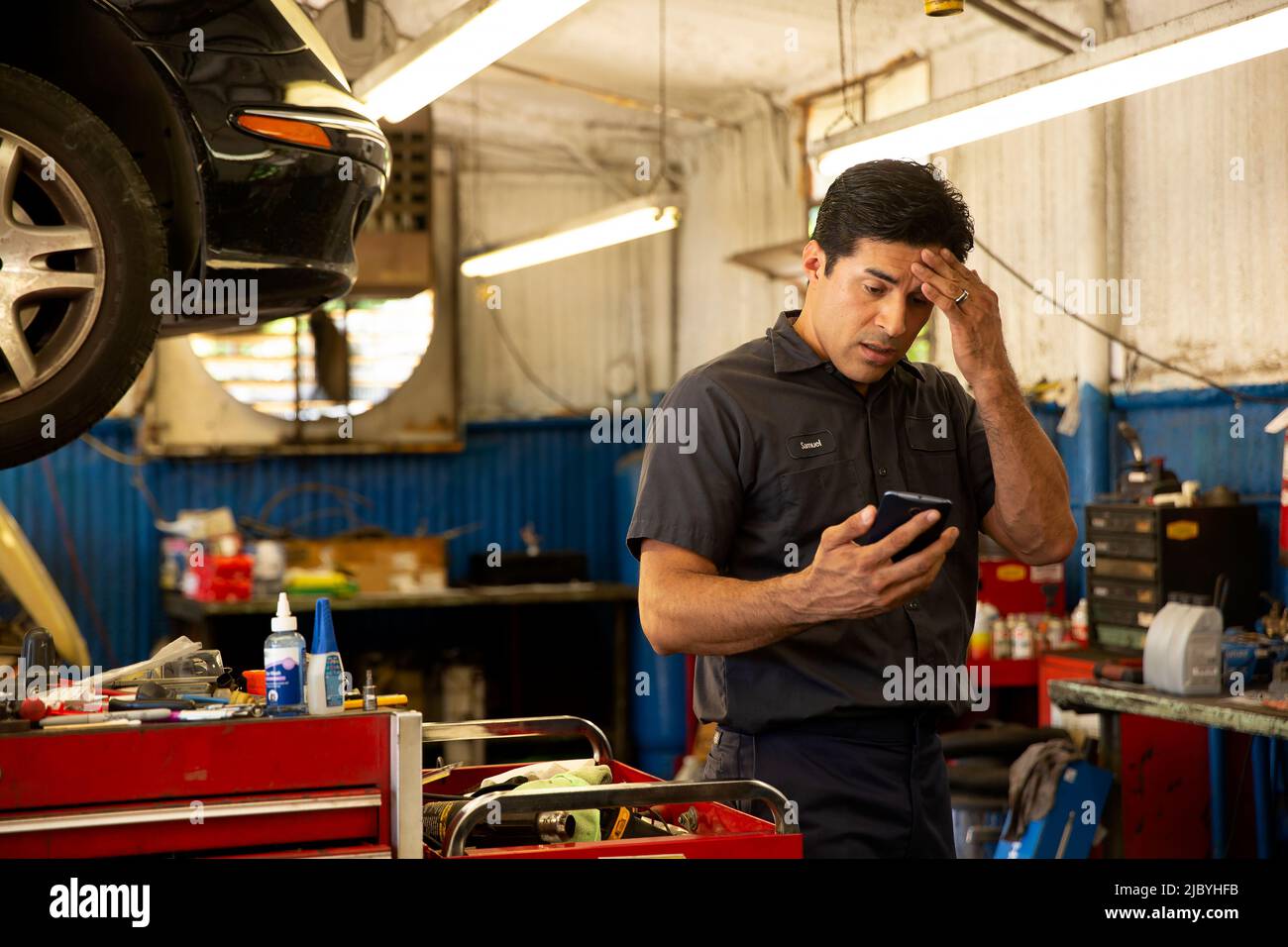 Hispanic car mechanic working in auto shop, having migraine headache
