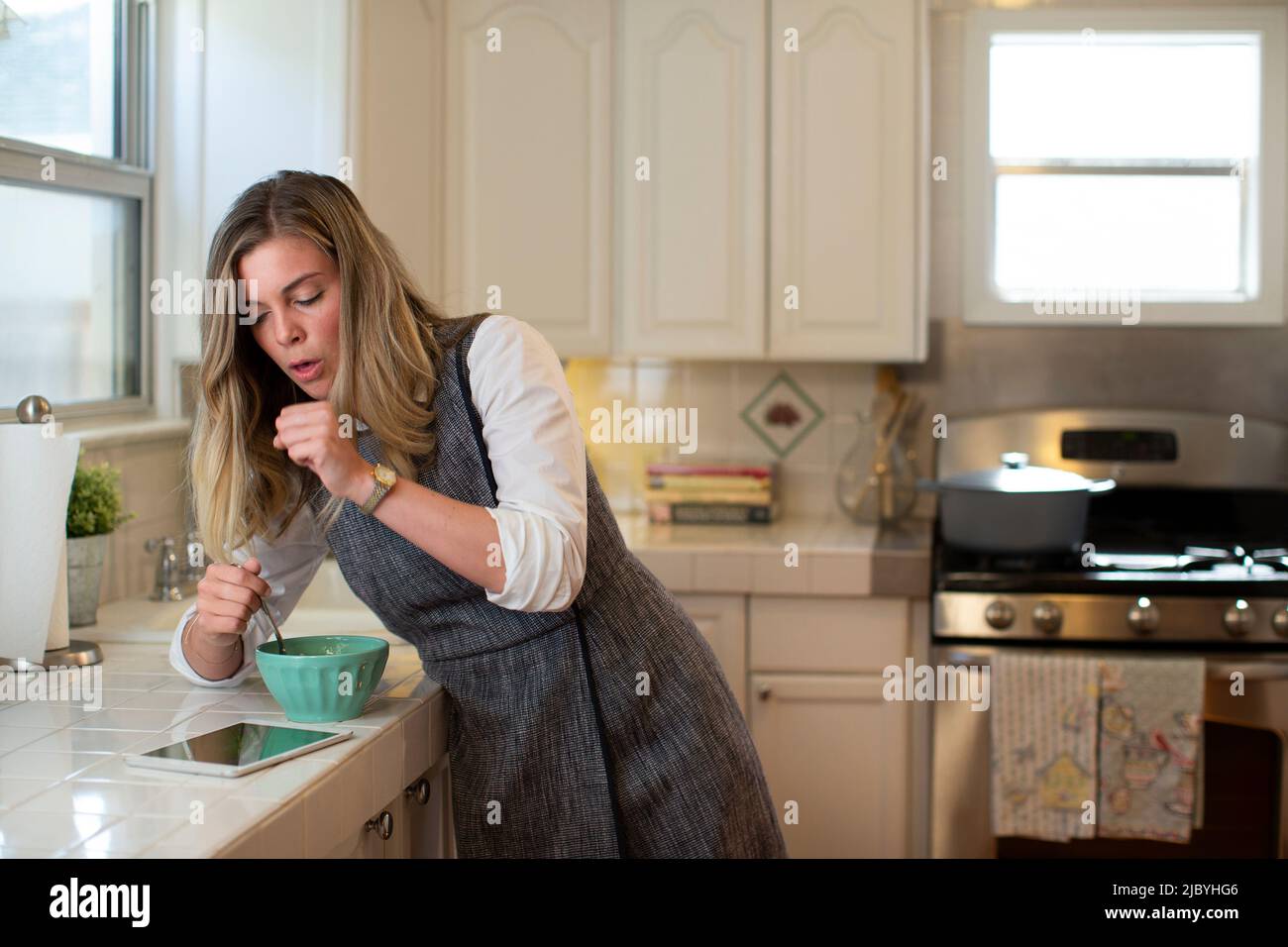 Coughing young woman in her kitchen, eating breakfast getting on her iPad Stock Photo