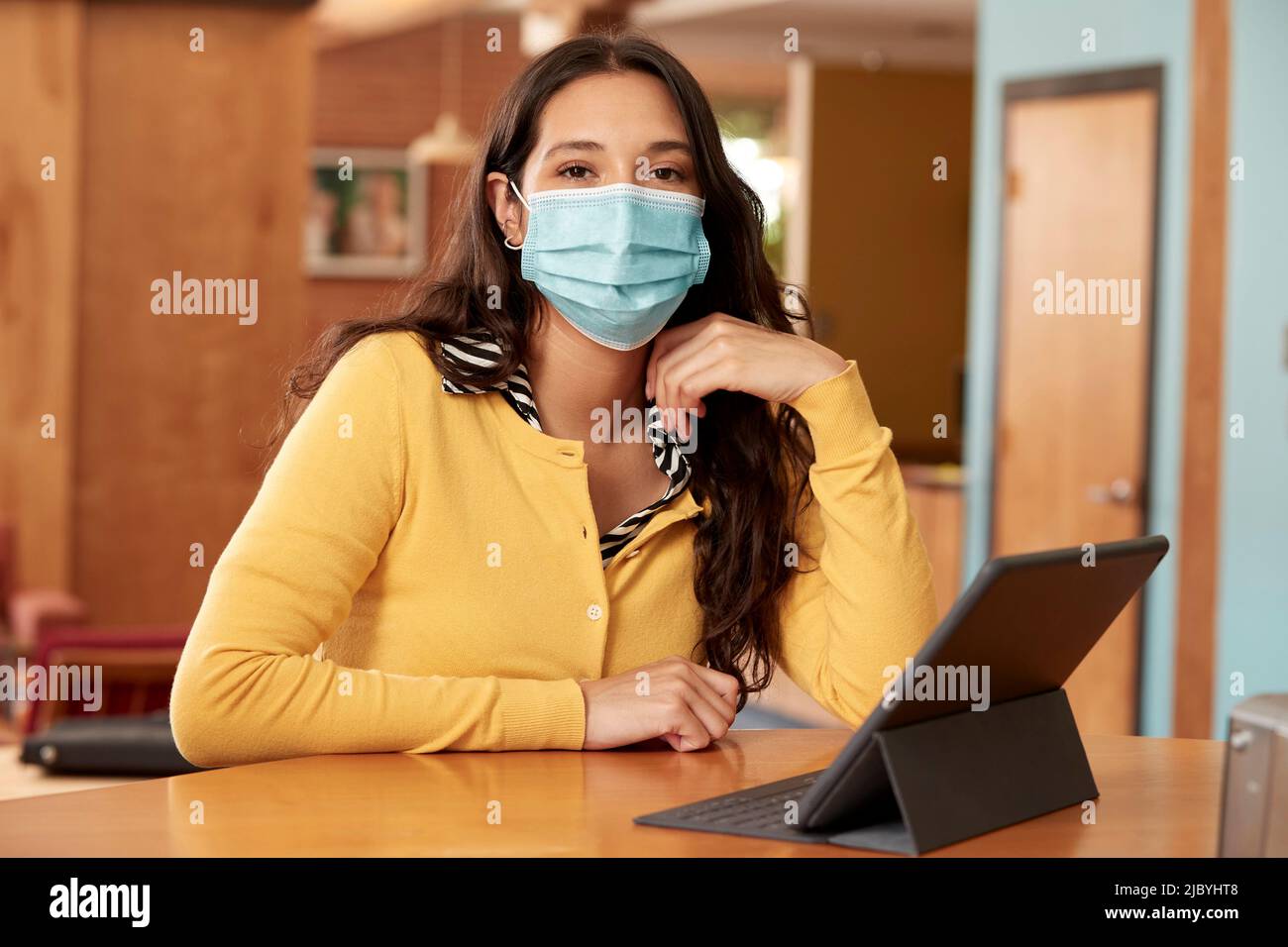 of young ethnic woman wearing yellow sweater with black and white striped blouse and face mask sitting at bar in kitchen of downtown loft with iPad Stock Photo Alamy