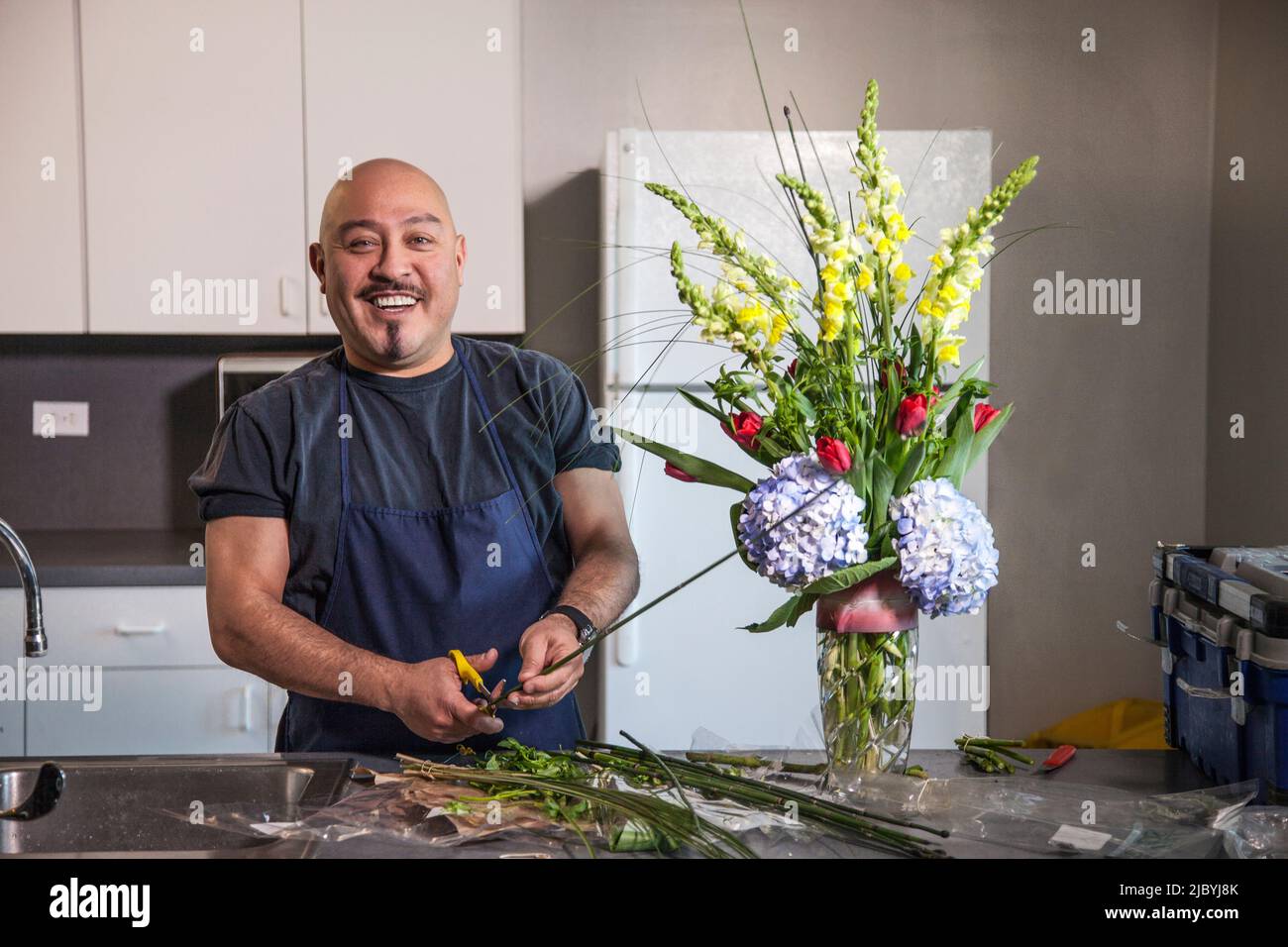 Smiling man arranging flowers in kitchen Stock Photo