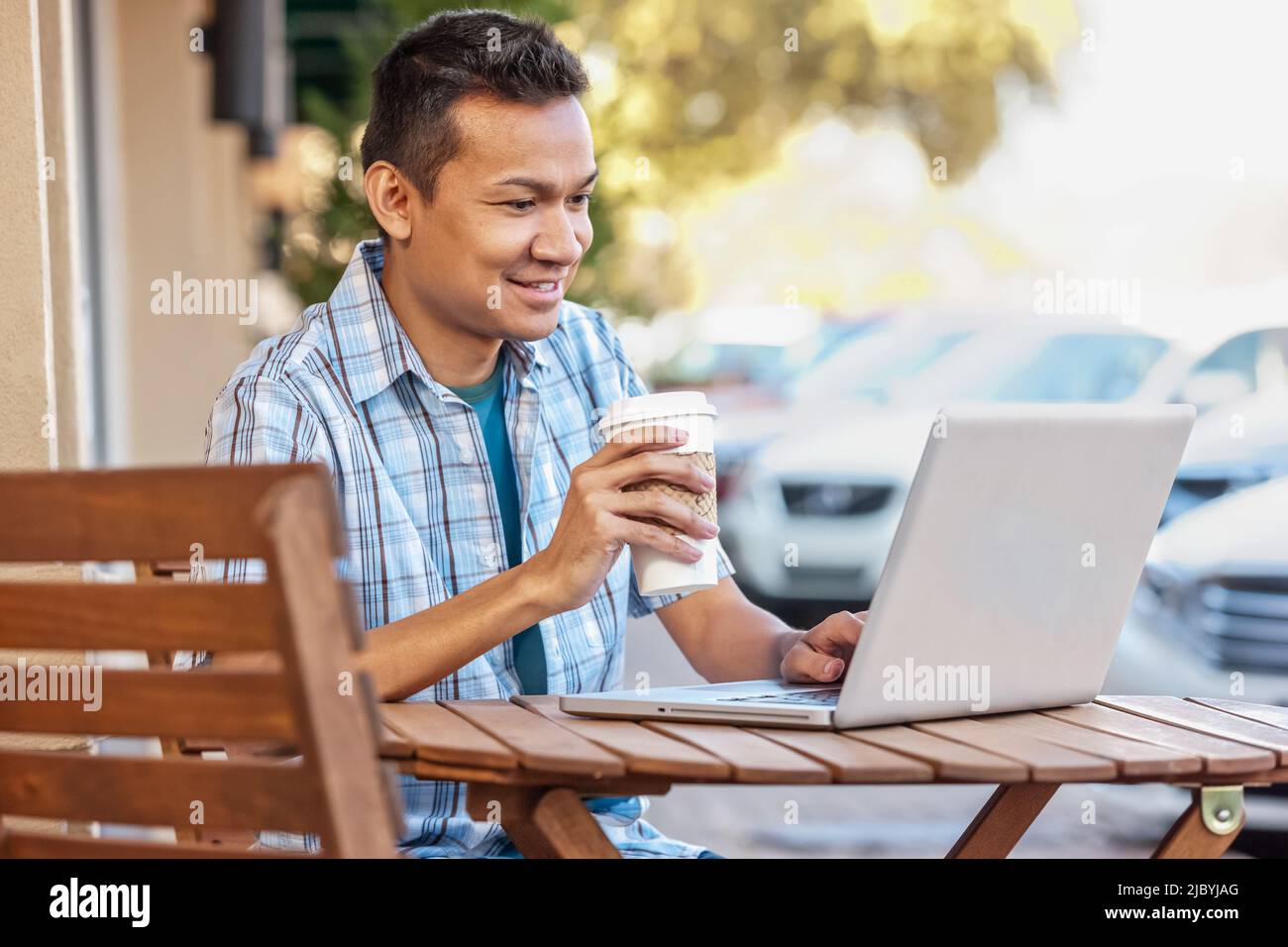 Malaysian man drinking coffee and using laptop at cafe Stock Photo
