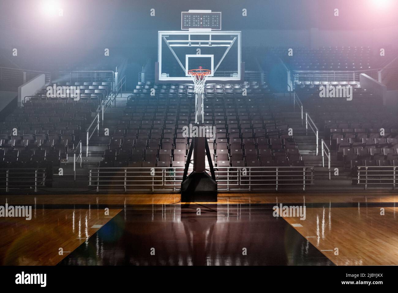 Empty basketball arena with dramatic lighting, view from free throw line in front of goal on the court Stock Photo