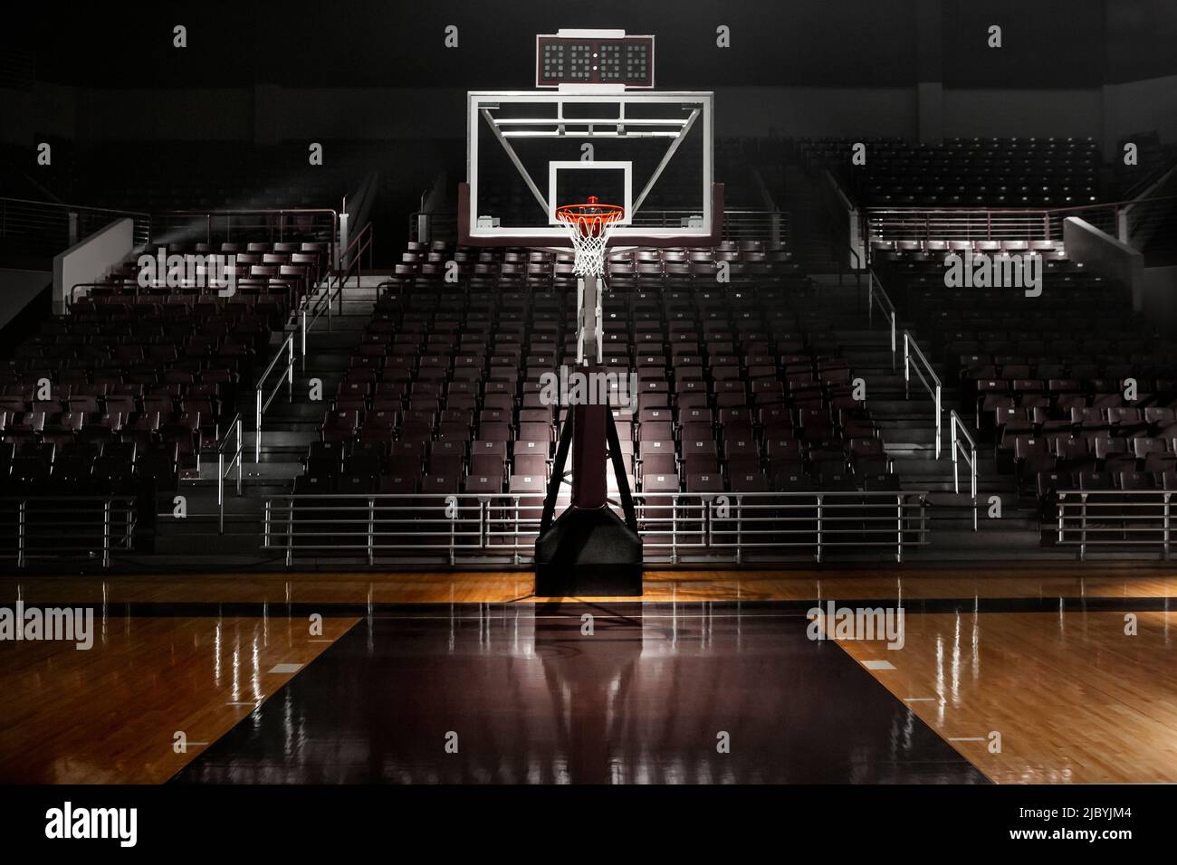 Empty basketball arena with dramatic lighting, view from free throw line in front of goal on the court Stock Photo