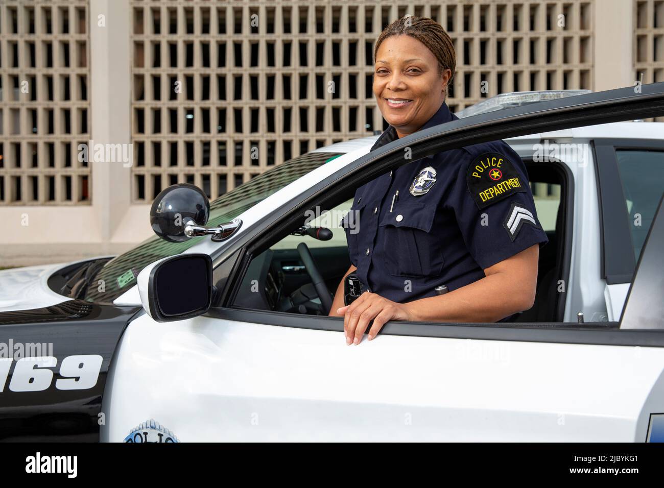 Policewoman standing in door of Police car looking towards camera smiling Stock Photo