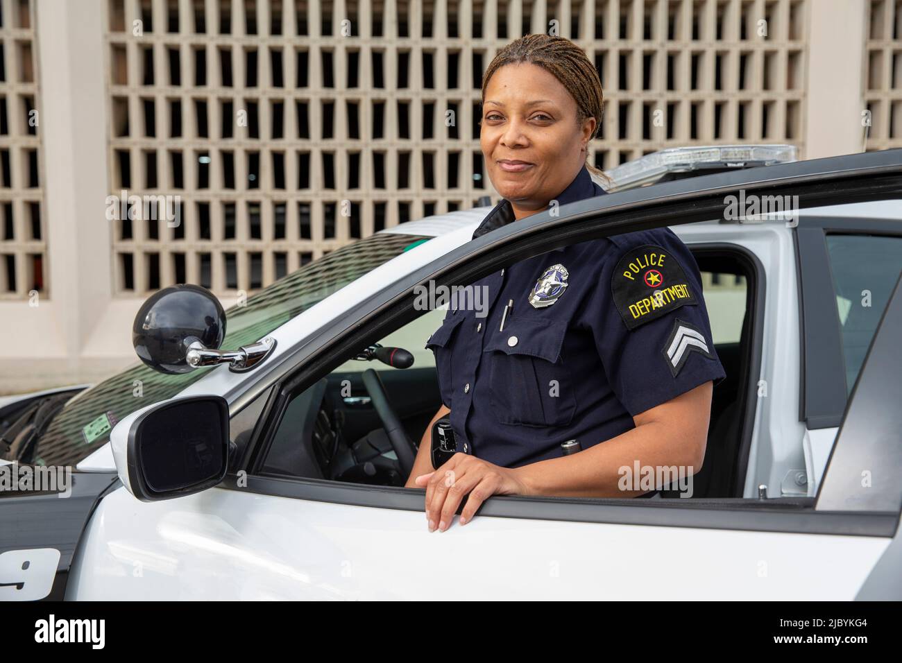 Policewoman standing in door of Police car looking towards camera smiling Stock Photo