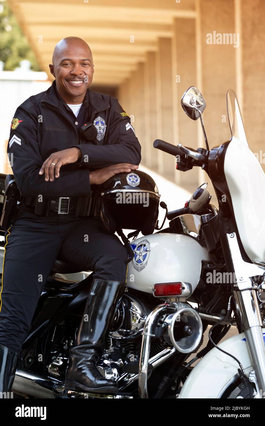 Portrait of Police officer sitting on his motorcycle outside looking towards camera smiling Stock Photo