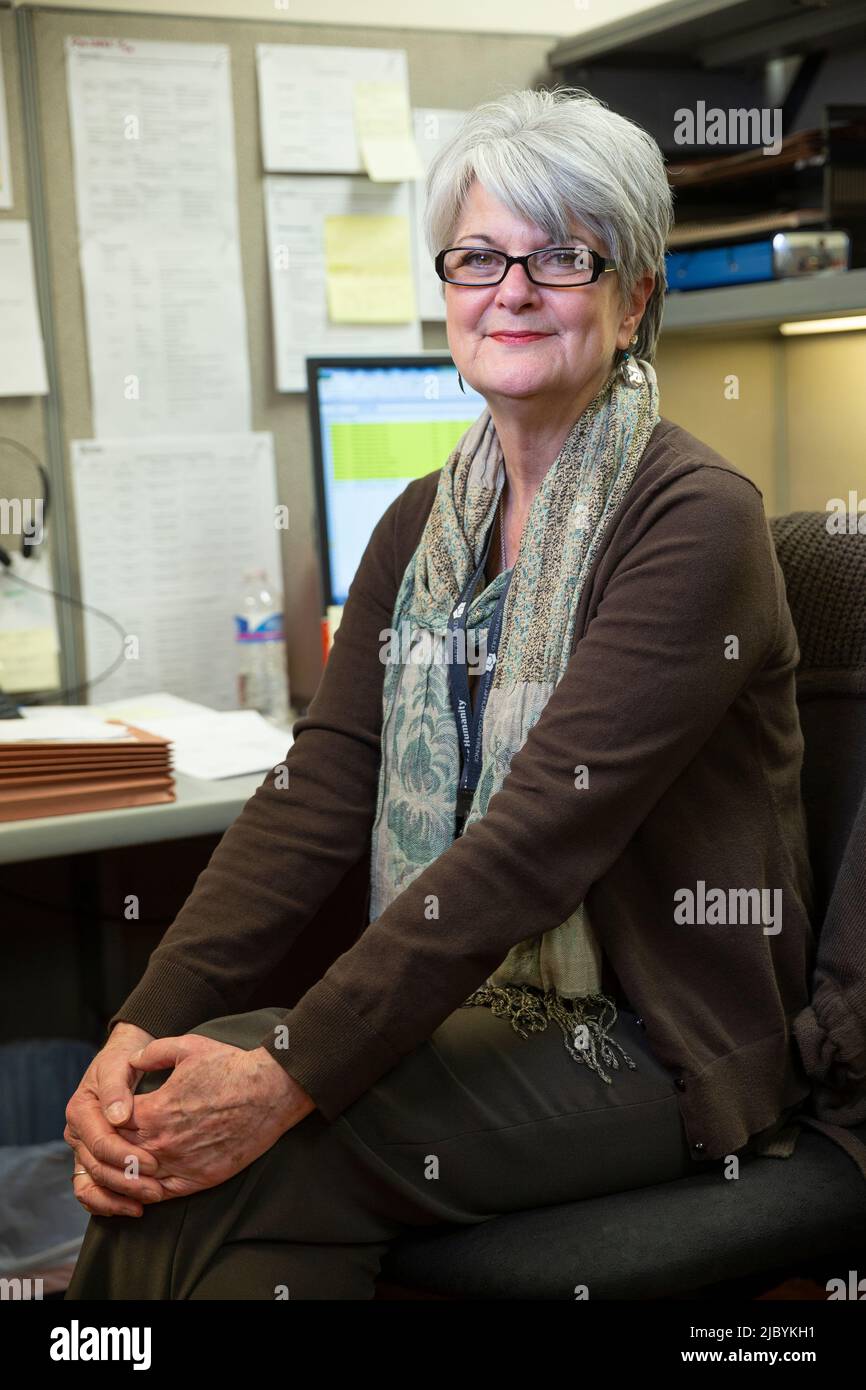 Portrait of woman sitting at her desk in office building with hands clasped on knees, looking at camera smiling Stock Photo