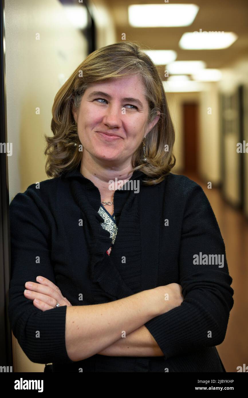 Portrait of middle aged woman with arms crossed in hallway of office building, smirking looking off camera Stock Photo