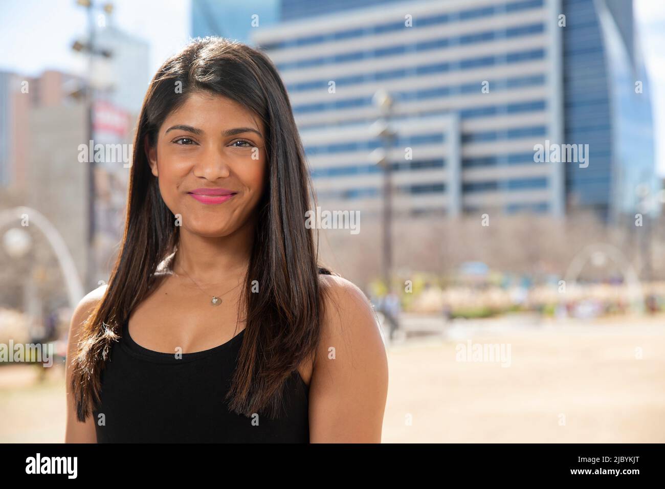Smiling portrait of young ethnic woman standing in park wearing black tank top Stock Photo