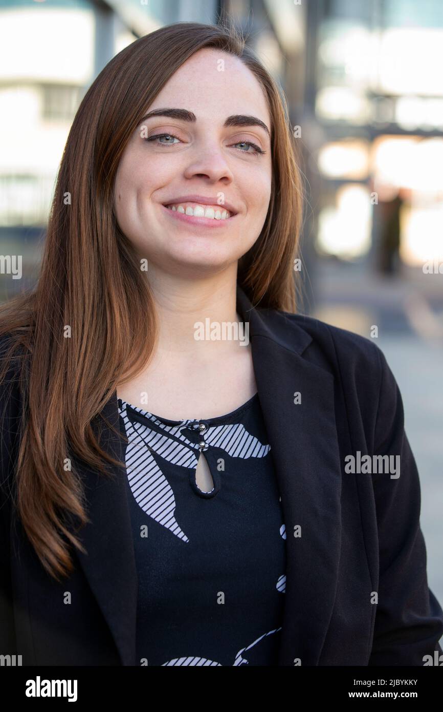 Portrait of woman with long hair standing outside in open shade, smiling looking at camera Stock Photo