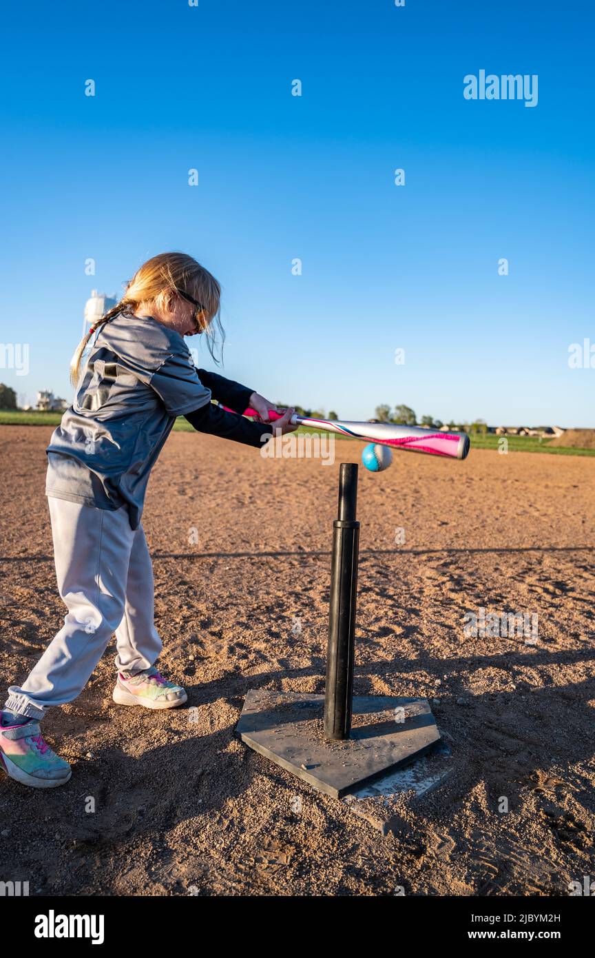 Young girl with a ponytail and sunglasses hitting a baseball off of a