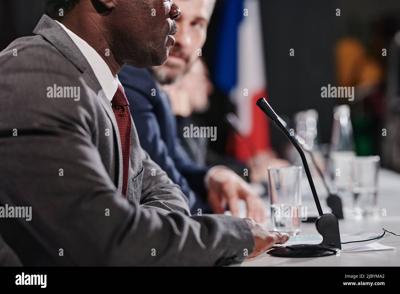 Close-up of African American speaker performing during press conference while sitting at table with other politicians Stock Photo