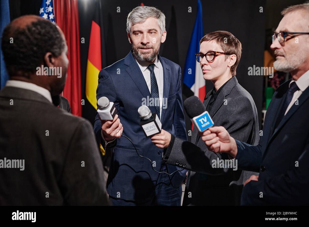 Group of journalists holding microphones standing opposite the speaker and taking an interview
