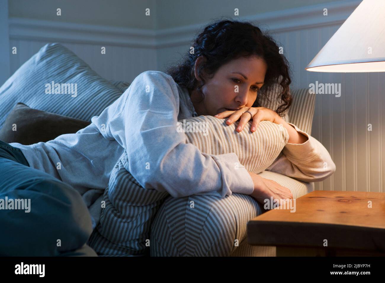 Worried Caucasian woman sitting on sofa Stock Photo