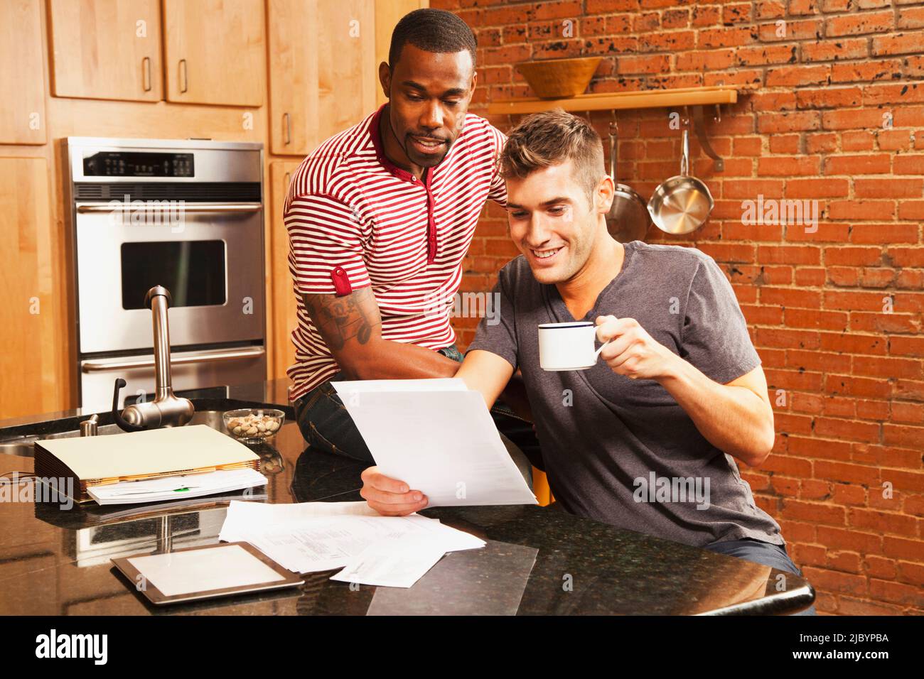 Gay couple looking at paperwork in kitchen Stock Photo
