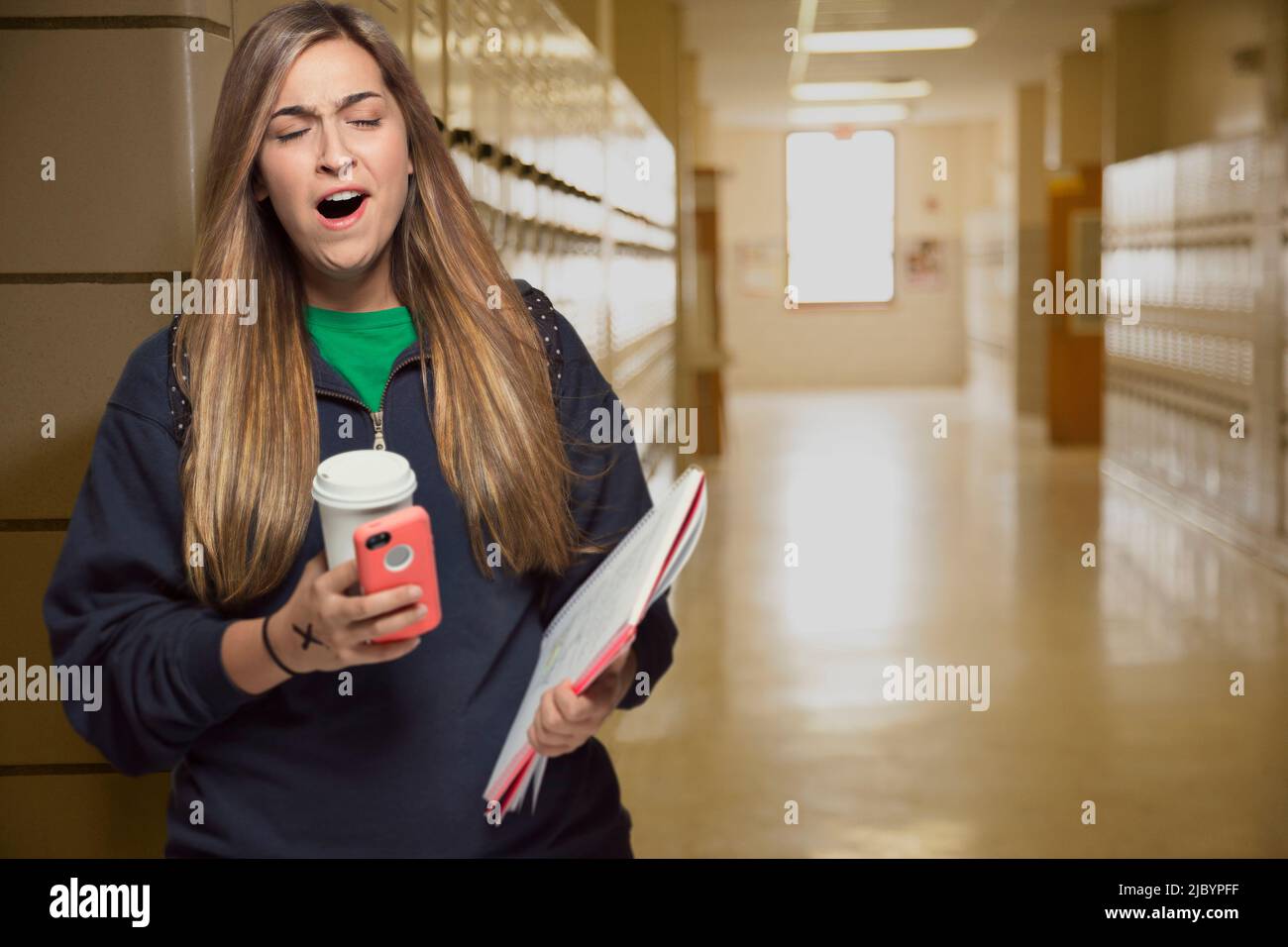 Middle Eastern student yawning in college hallway Stock Photo