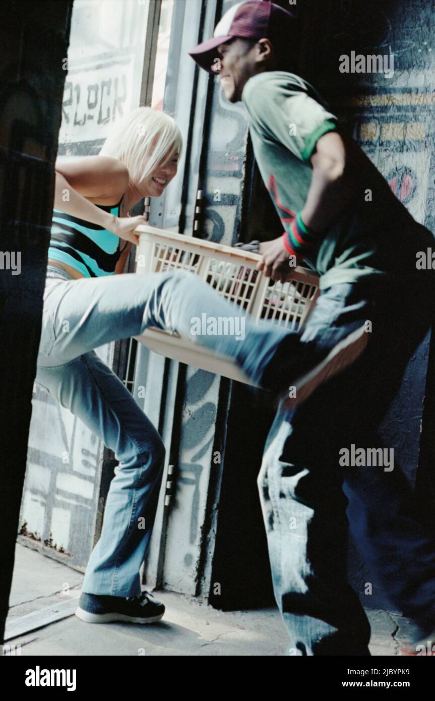 Asian girl kicking African boyfriend holding laundry basket Stock Photo