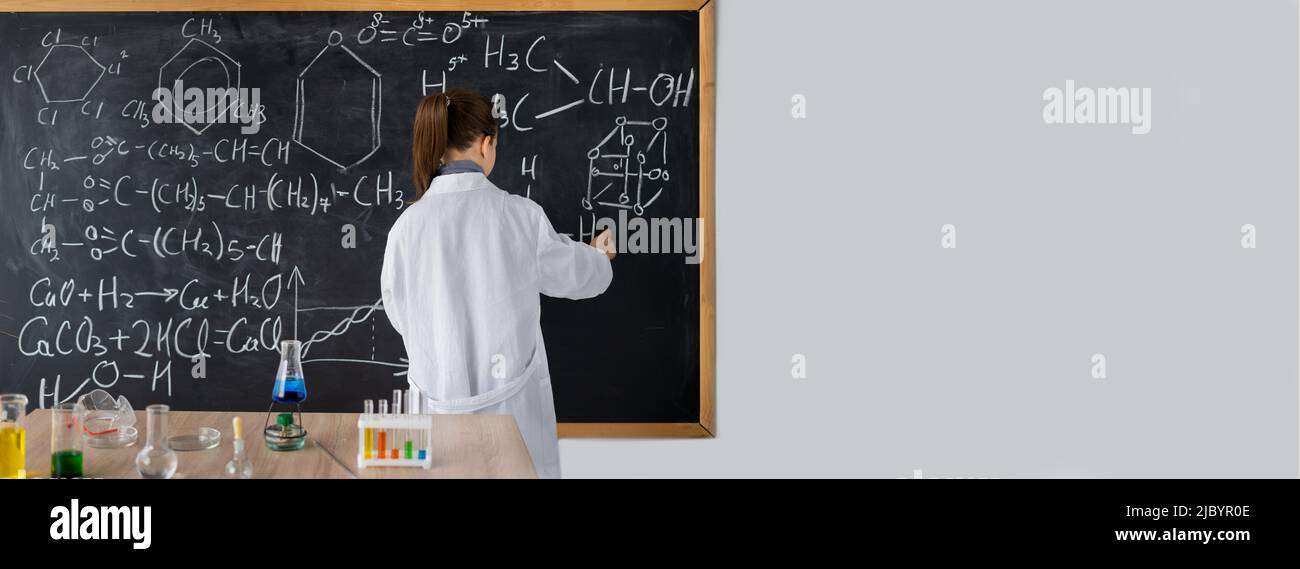 Girl student writing with chalk on a blackboard, chemical formulas on a
