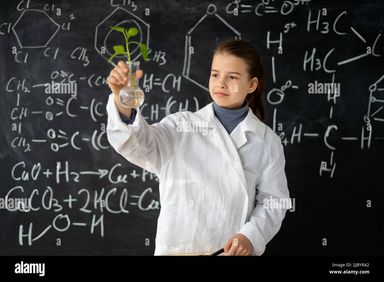 Young student studying small plant in flask in elementary sciences
