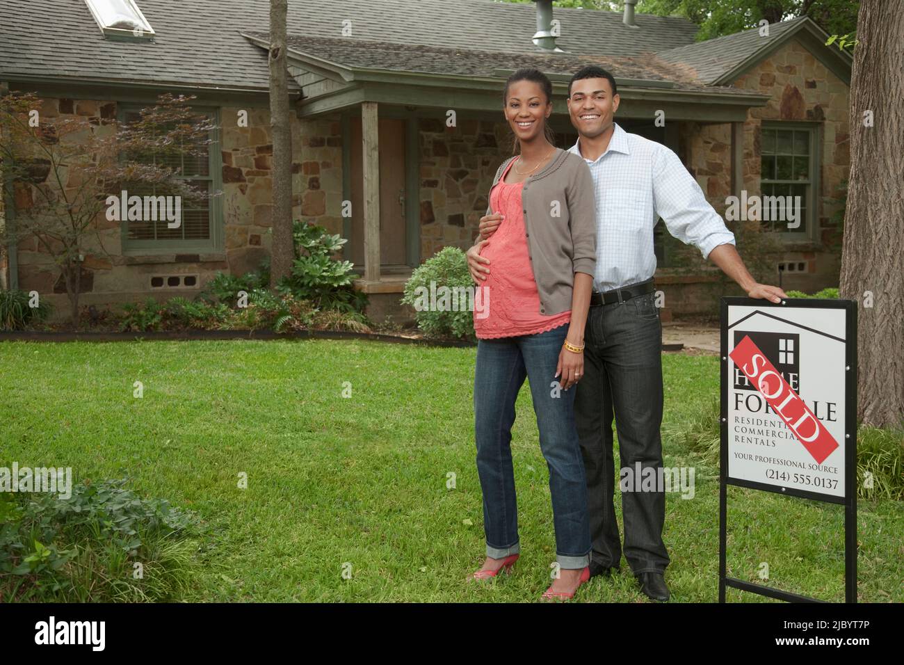 Couple standing in yard with sold sign Stock Photo - Alamy