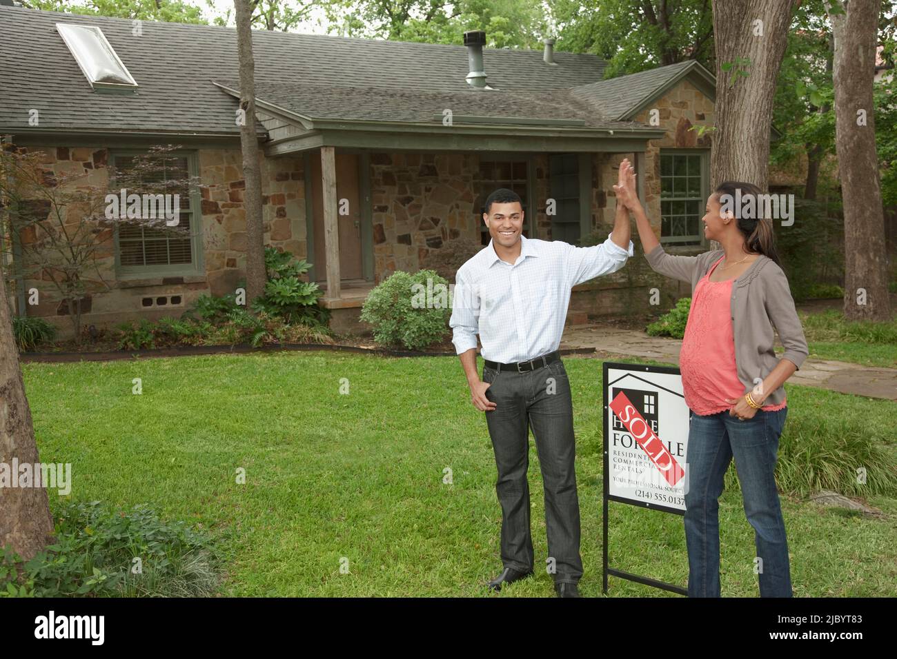 Couple standing in yard with sold sign Stock Photo - Alamy