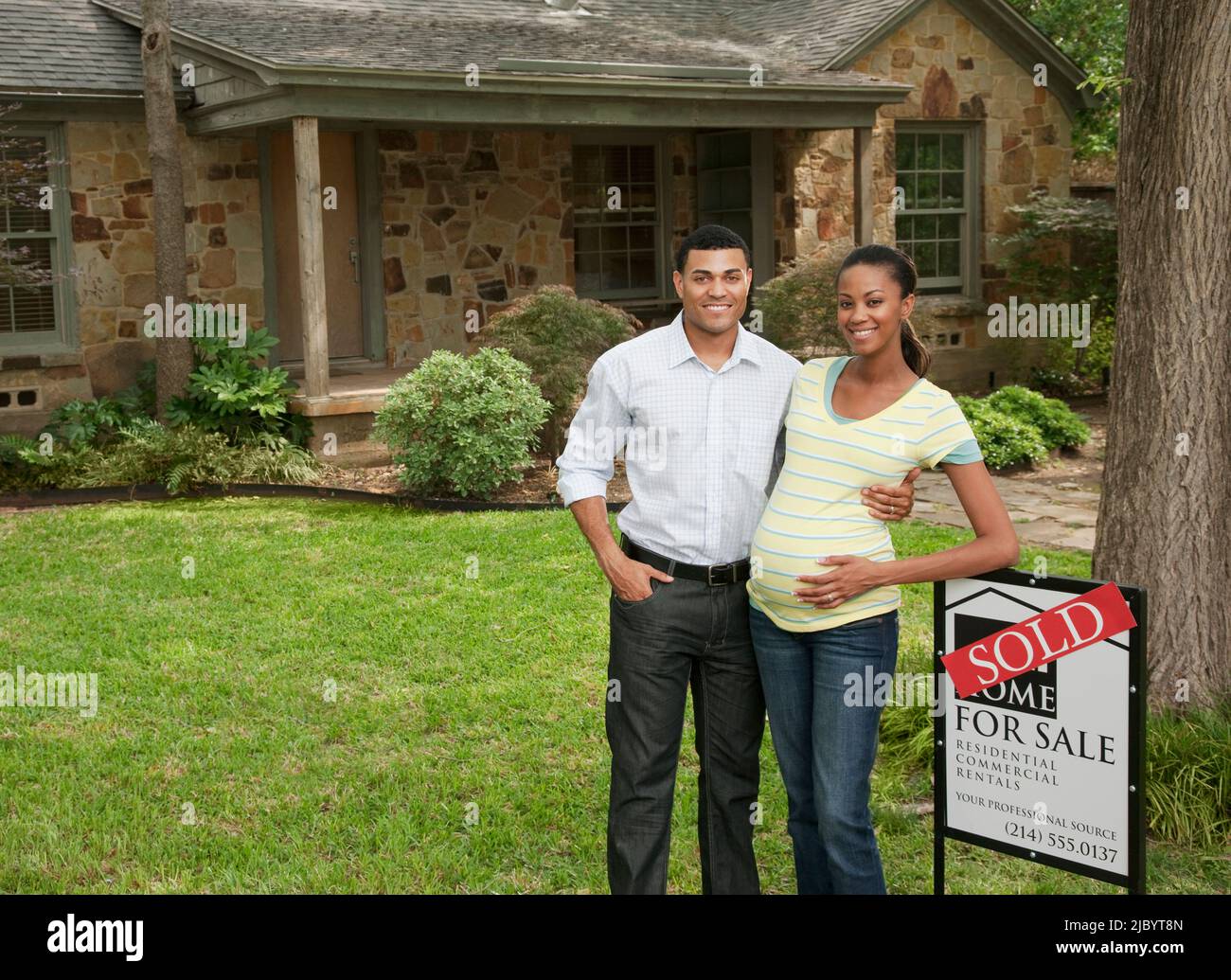 Couple standing in yard next to sold sign Stock Photo - Alamy